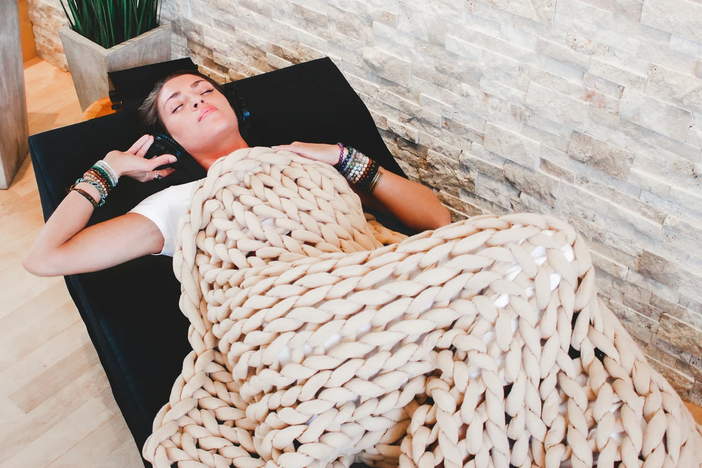 Manufacturer photograph of a person resting on the Sensory Lounge with headphones and a knitted blanket